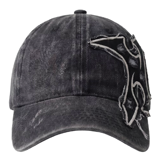 A black acid-wash distressed baseball cap featuring a large, frayed, abstract embroidered patch on the side, shown against a plain white background.